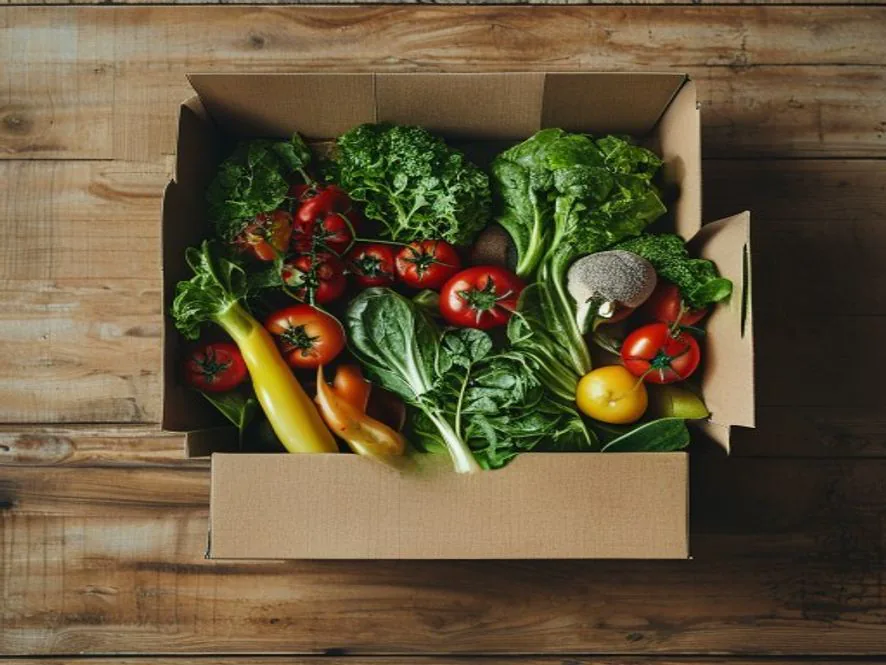 Fresh vegetables being arranged inside a cardboard grocery box
